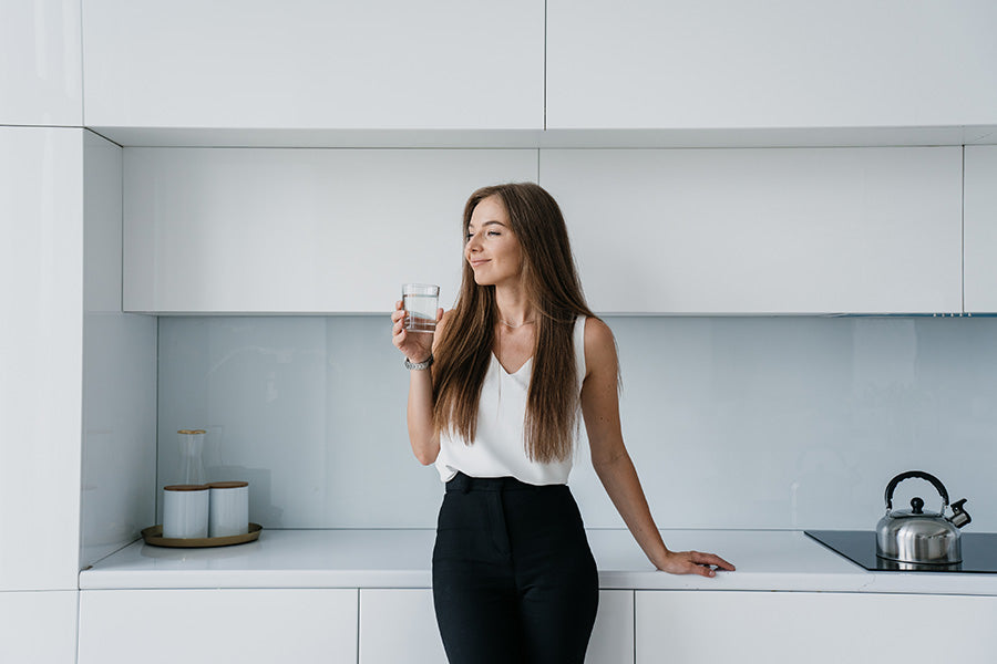 Attractive healthy woman holding a glass of hydrogen rich water in a modern kitchen