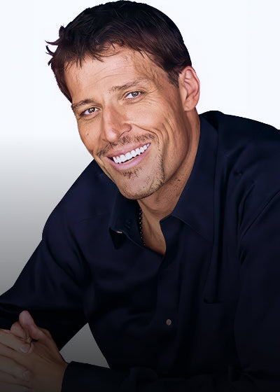 Author and speaker Tony Robbins wearing a dark blue shirt against a white background, smiling.
