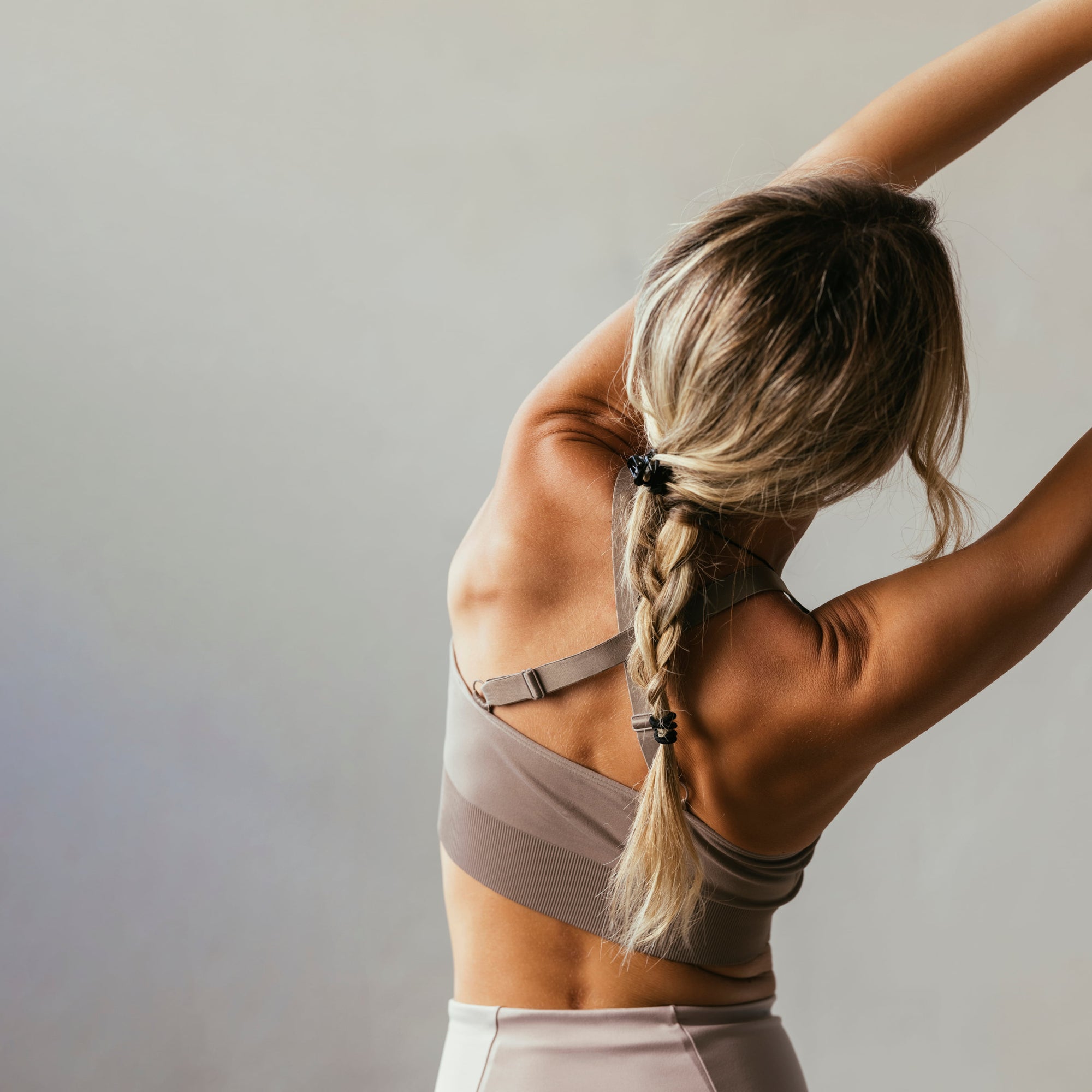 Fit aging woman in sportswear stretching her body against neutral background