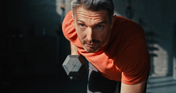 fit aging man doing bent row curl with a dumbbell in a gym setting