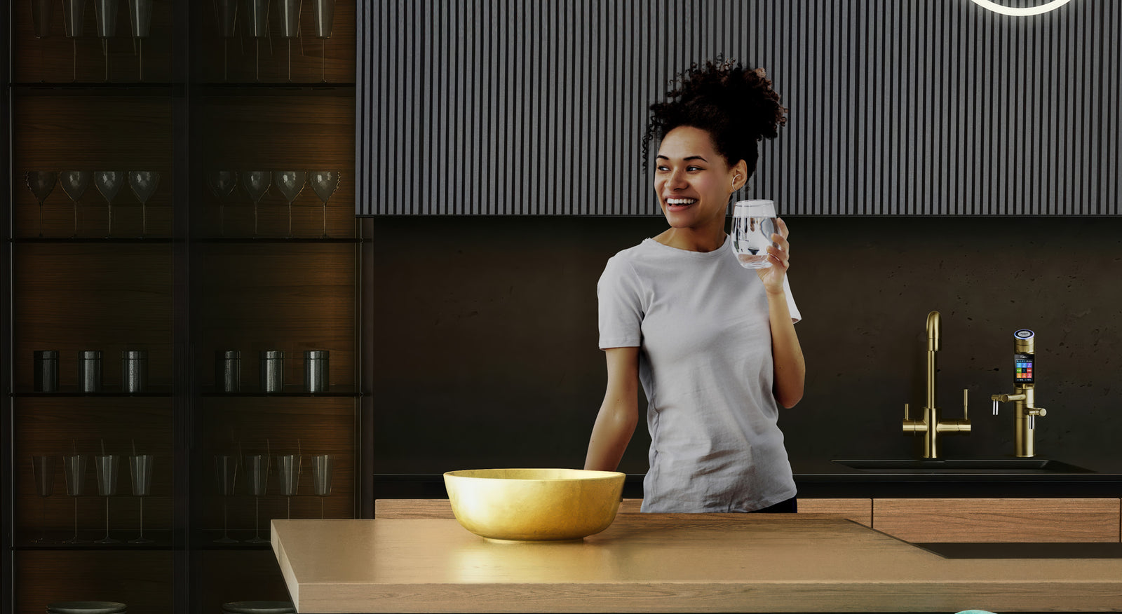 A woman smiling holding a glass of water in a luxurious modern kitchen with a UCE Tyent water ionizer in the background.